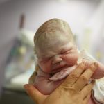 Cloe-up on newborn baby held by midwife