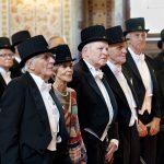 Finklädda hedersdoktorer i frack och hatt stående i rad i universitetets vacka aula.